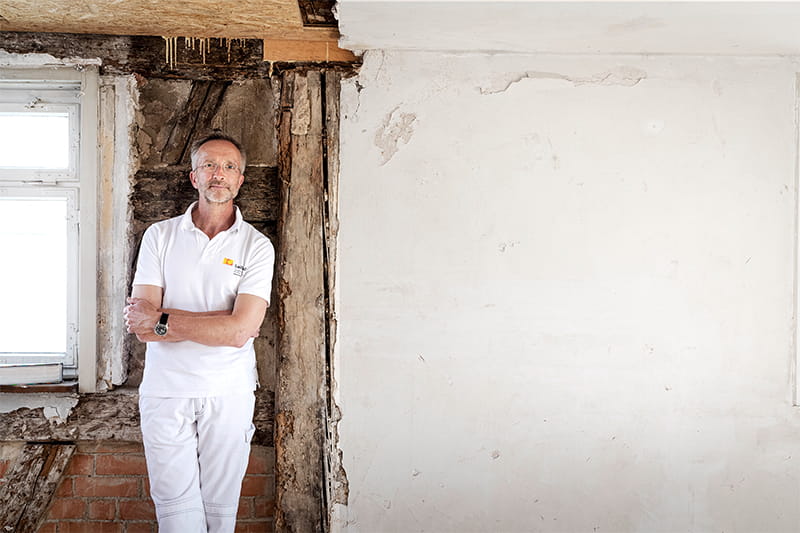 Manfred Schuler, Malermeister und Restaurator vor der Wand des zu restaurierenden Fachwerkhauses