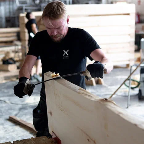 A sauna builder stripping the wood with a knife.